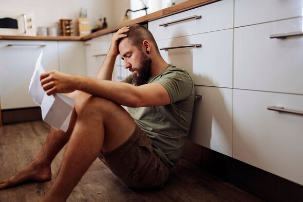 A bearded man on a kitchen floor holding papers
