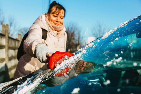 A woman clears ice from her car windshield