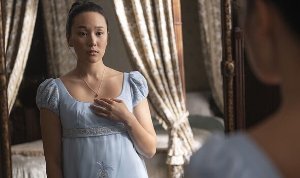 A woman in a blue dress looks sad as she clutches a necklace