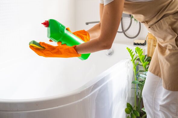 Woman in rubber gloves and apron manually washes bathtub is in bathroom of house with sponge cleaner and cleaning agent in a bottle. Restoring order,