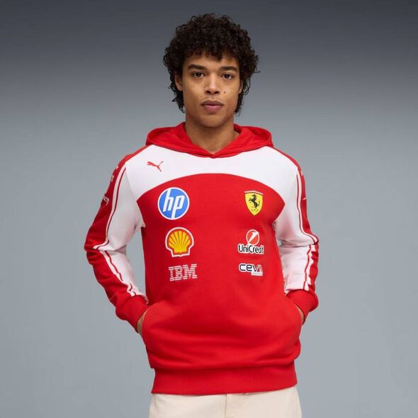 An individual is dressed in a red and white hoodie featuring various logos, including those of HP, Shell, and Ferrari, along wit