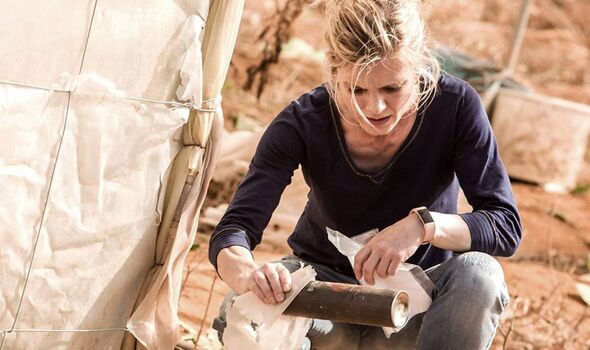 An individual is engaged in an outdoor activity, sitting and meticulously examining a piece of paper, while dressed in a dark lo