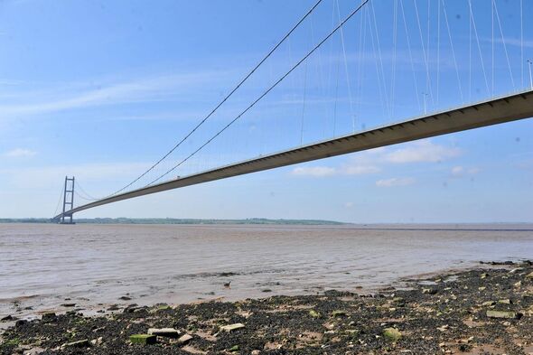 A suspension bridge with a long, arched span extending over a body of water, with rocky shorelines and a clear blue sky in the b