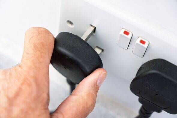 Hand inserting black electrical plug into white wall socket with switches in indoor home setting