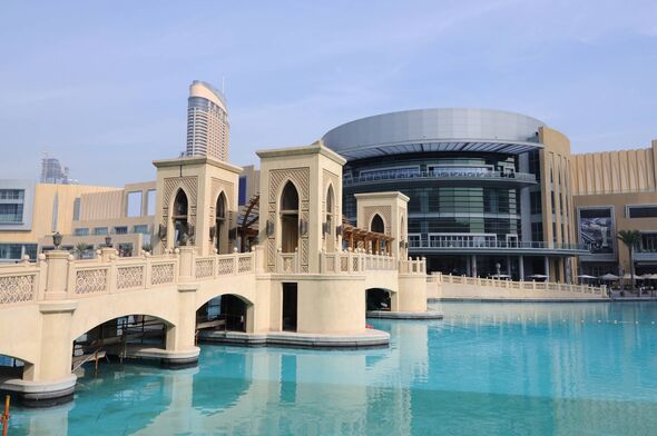 An architecturally designed bridge over a water body with a large building in the background.