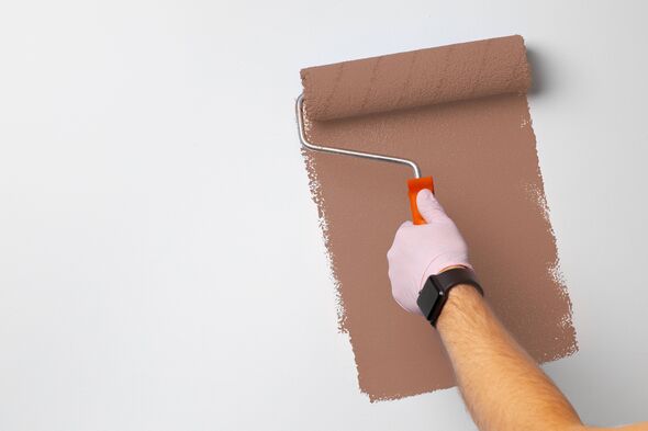 A hand holds a roller brush while painting a wall in a room.