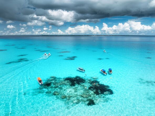 Aerial view of colorful boats and yachts in clear water on sunny summer day. Mnemba island, Zanzibar. Top view of sandbank in low tide, blue sea, swim