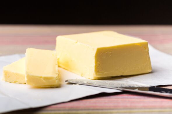 Close-up of a block of butter and sliced pieces on parchment paper with a knife, ready for use