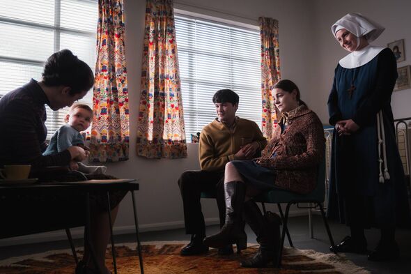 Several individuals are gathered in a room, possibly engaged in a discussion. One person is seated at a desk, focusing on a docu