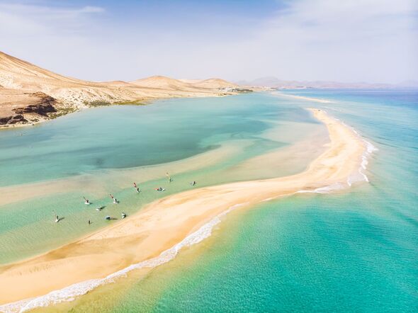 Aerial view of beach in Fuerteventura island with windsurfers learning windsurfing in blue turquoise water during summer vacation holidays.