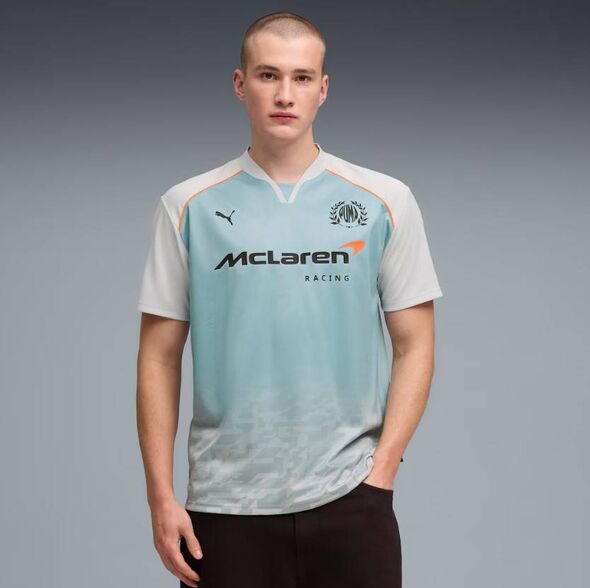 An individual stands against a gray backdrop, wearing a light blue and white sports jersey with the word