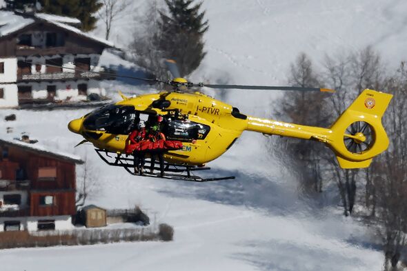 A yellow rescue helicopter hovers over a snowy landscape, near residential buildings. The helicopter is equipped with medical eq