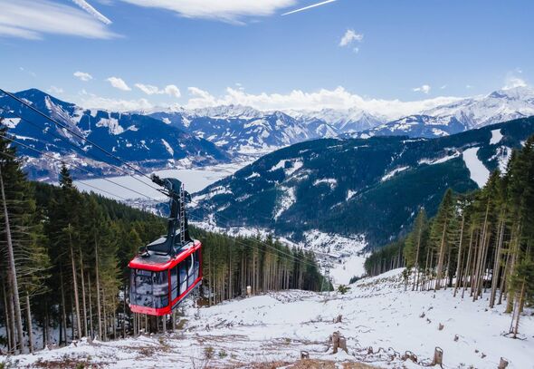 A vibrant red cable car is suspended mid-air, traversing a snow-covered mountain landscape. The backdrop features majestic snow-