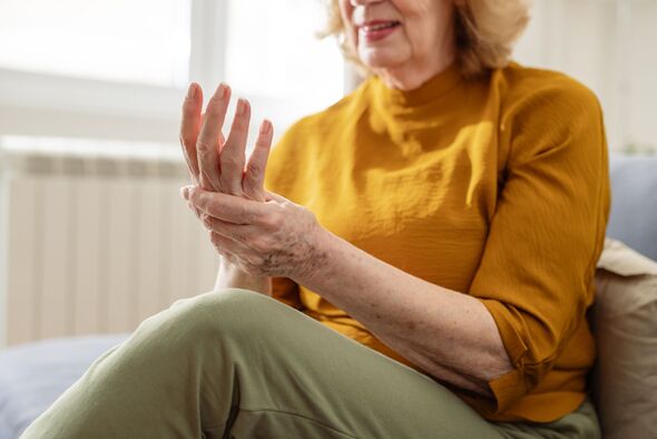 Senior woman seated at home, experiencing hand pain and discomfort