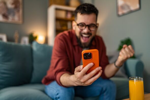 Excited man using smart phone at home and celebrating.