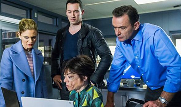 A group of individuals are gathered around a laptop in a room, attentively observing the screen. One person is dressed in a blue