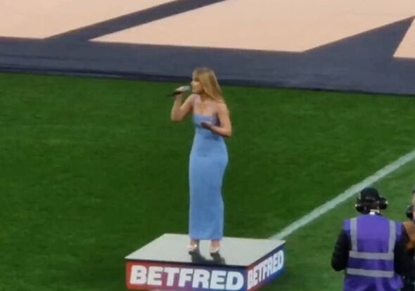 Camilla Kerslake singing at the Rugby Super League final at Wembley Stadium while wearing a blue dress
