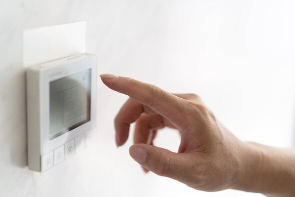 A hand is pressing a button on a white thermostat