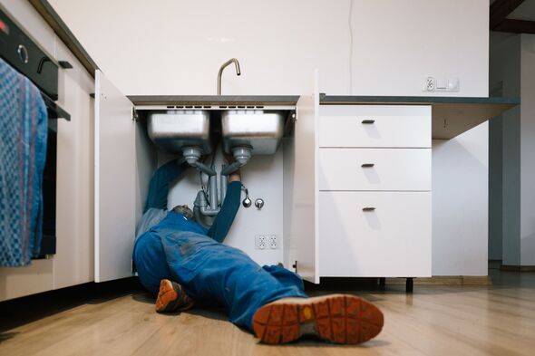 A plumber repairs a blocked drain in a kitchen