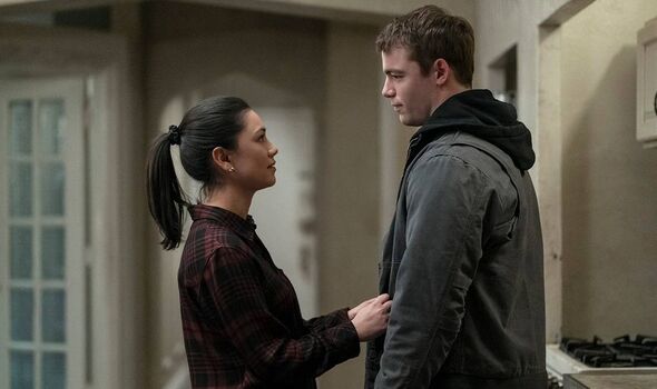 An individual in a black long-sleeve top with a ponytail stands facing another individual dressed in a grey hoodie jacket, both