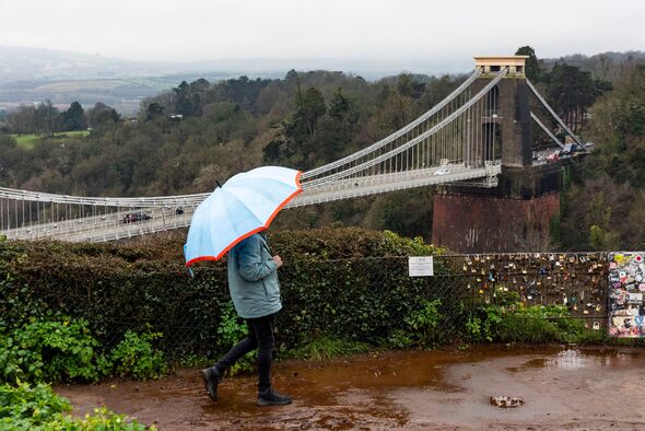 Person with umbrella in rain in front of bridge