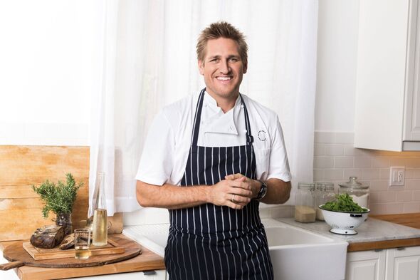 An individual, presumably a chef, stands in a kitchen wearing a black apron. They are positioned in front of a countertop adorne