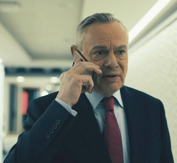 An individual in formal attire, consisting of a suit and tie, is engaged in a conversation on a mobile phone, his expression ind