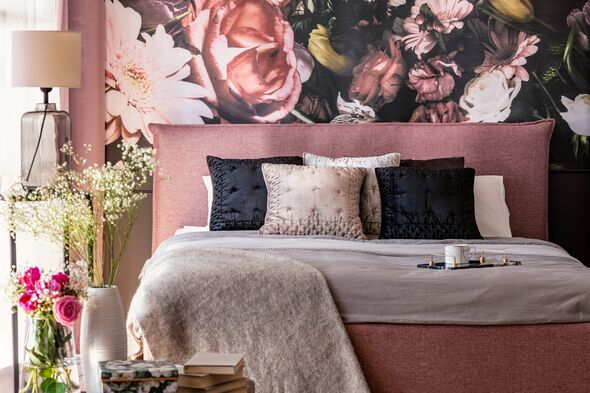 Pink and grey bed with cushions in patterned bedroom interior with flowers and lamp. Real photo
