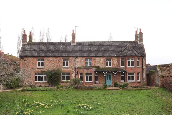 An image depicts a large traditional house with a black roof and several chimneys. The house is surrounded by a well-maintained