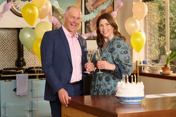An adult male and an adult female are standing next to each other, smiling and posing for a photograph in a decorated room.
