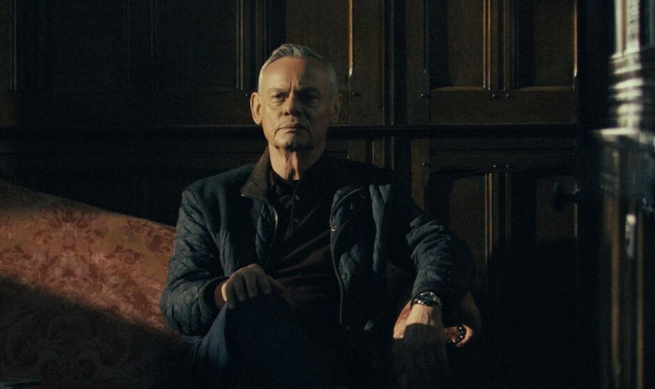 Martin Clunes in character as Huw Edwards sits on a four poster bed