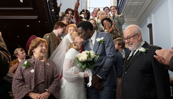 Cyril and Rosalind kiss followign their weddign as their friends and neighbours look on smiling