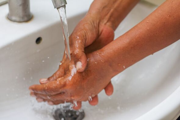 Washing Hands Under Running Water in Bathroom Sink
