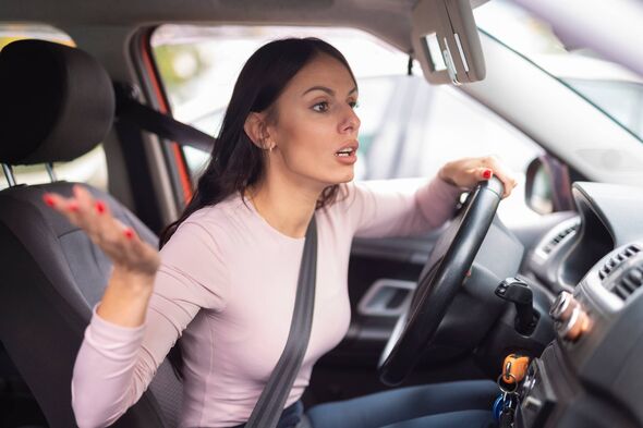 Young woman in the driver’s seat leaning forward with an exasperated expression, raising her hand in frustration as if reacting