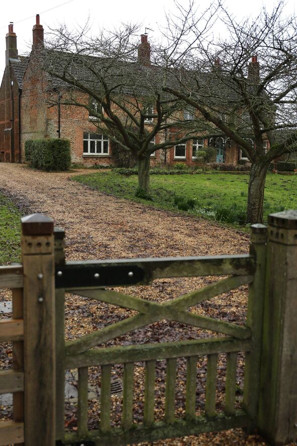 An image depicting a traditional house surrounded by lush greenery. The driveway leading to the house is flanked by trees, and t