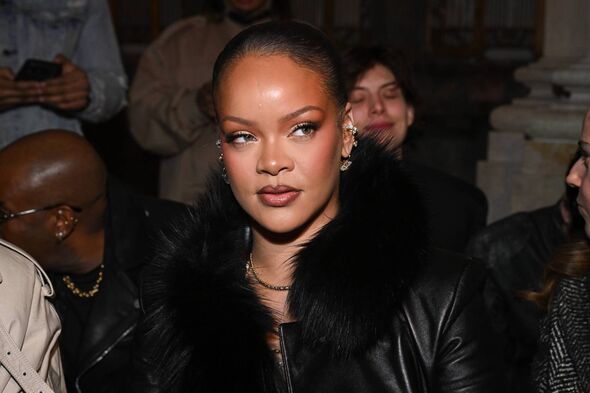 An individual, dressed in a black leather jacket with a fur collar, stands amidst a group of people, appearing to be engaged in