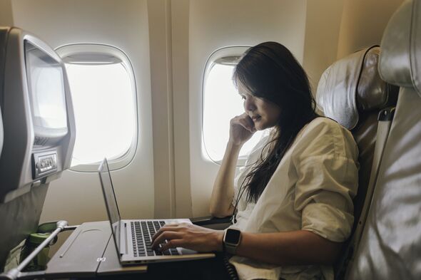adult businesswoman using laptop in economy class airplane cabin