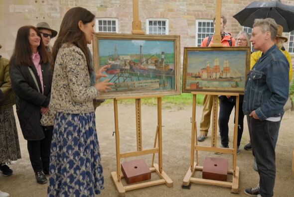 Individuals are gathered around two wooden easels displaying paintings in a setting that appears to be an outdoor exhibition, wi
