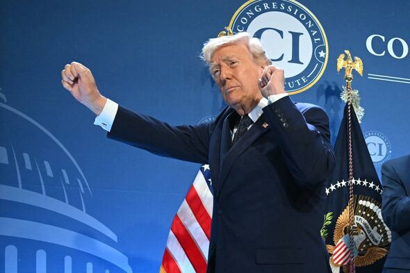 An individual in formal attire, possibly engaged in a public address, is positioned before a backdrop featuring a stylized depic