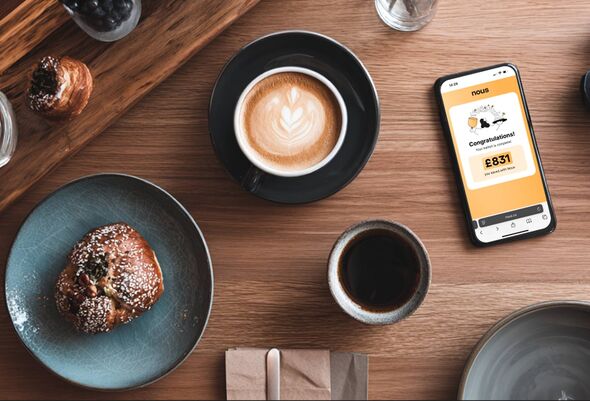 The nous.co app on a phone beside a cup of coffee.