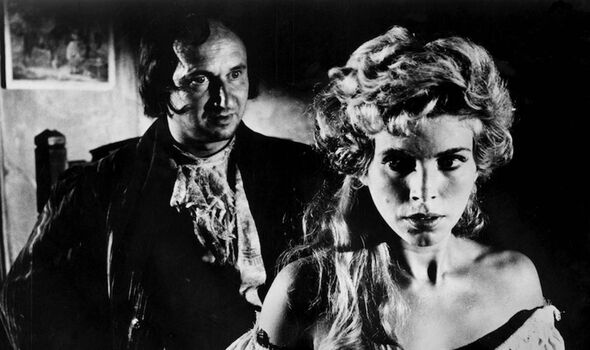 A monochromatic image depicts an individual with a stern expression, attired in a dark suit, standing next to another individual