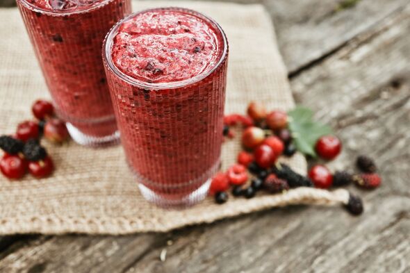 Refreshing berry smoothie in tall glasses with fresh fruits on rustic wooden table
