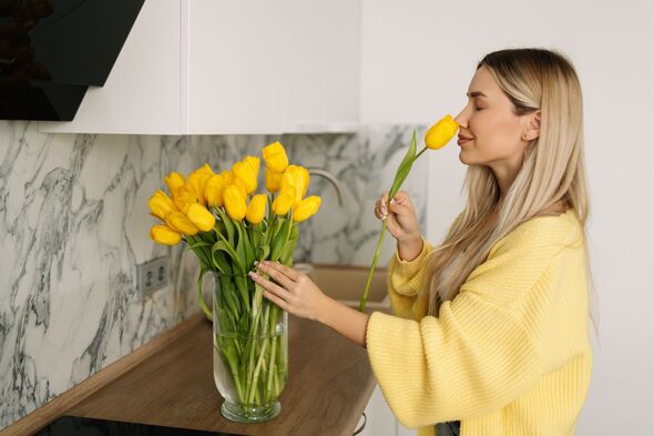 A beautiful woman with long hair in a yellow cardigan is pruning flowers at home, changing the water and taking care of them in the kitchen at home. A