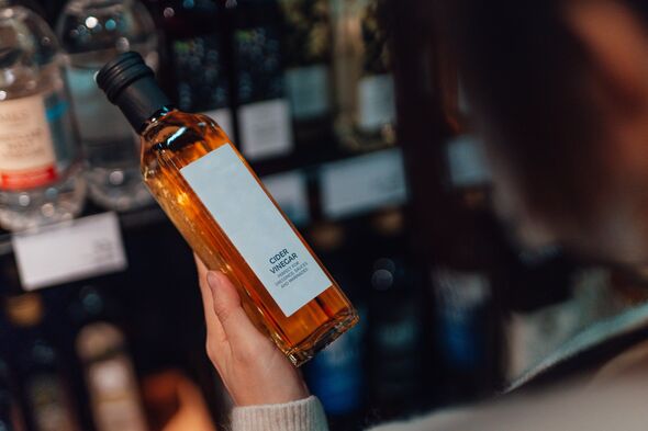 Close-up of young woman doing grocery shopping in supermarket, holding a bottle of vinegar