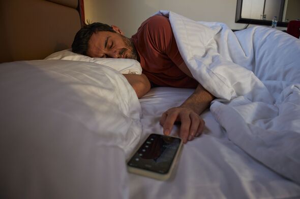 Man sleeping in bed next to ringing alarm phone