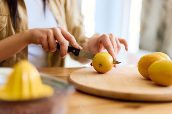 Woman cutting fresh lemon on wooden board preparing healthy drink