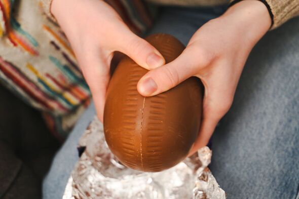 Close-up hands opening a chocolate egg.
