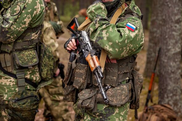 Close up hands russian soldier man dressed military camouflage uniform holds weapon in woodland at soldiers background. Male border guard in country b