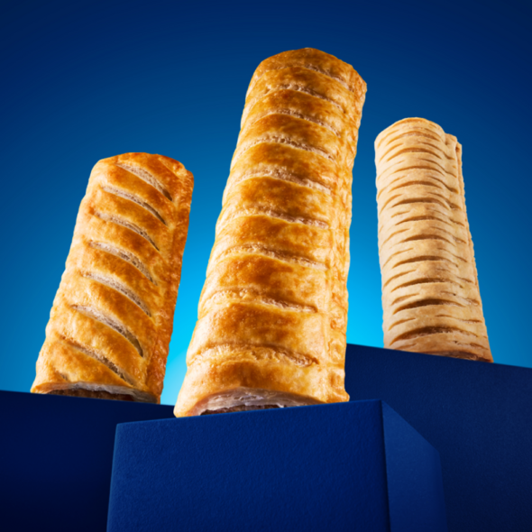 Three Greggs sausage rolls stood up against a blue background