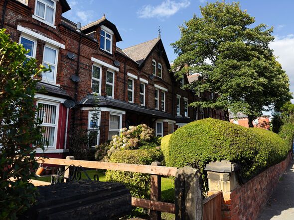 Row of red brick terrace houses in Manchester with hedges, trees and blue sky